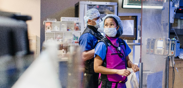 A doctor stands in scrubs with a surgical mask on