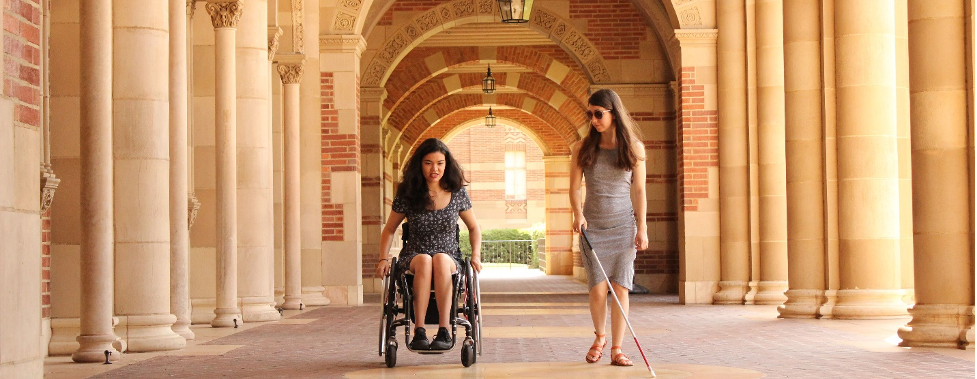 A student in a wheelchair and a blind student walking on a college campus
